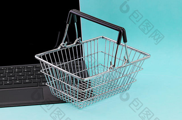 互联网购物的概念是一台笔记本电脑，在蓝色背景下，键盘上有一个迷你购物篮
