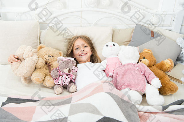 女孩穿睡衣。睡觉前玩软玩具。和玩具睡觉。舒适的卧室。睡前放松。女孩喜欢晚上玩玩具。孩子躺在有玩具枕头毯背景的床上。