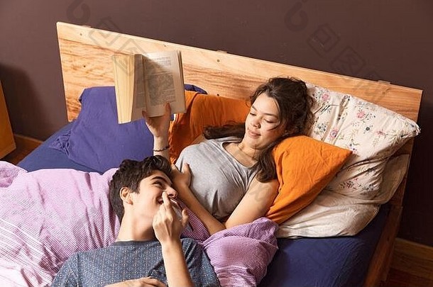 这对年轻夫妇躺在床上。他们一边玩一边看电话