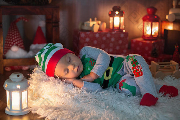 可爱的蹒跚学步的孩子，男孩，睡觉时带着很多玩具，打扮得像个小精灵，身边有圣诞装饰