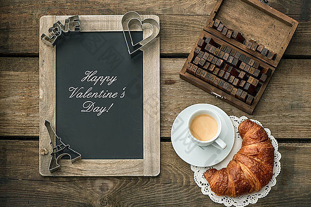 一杯黑咖啡，配牛角面包、黑板和心形装饰，背景为乡村木质。浪漫的情人节假期