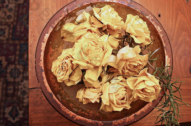 木制桌子上的玻璃碗中的干黄玫瑰，取自上方