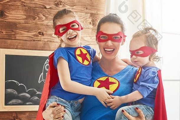 妈妈和她的孩子们一起玩。穿着超级<strong>英雄</strong>服装的女孩和妈妈。妈妈和孩子们玩得很开心，微笑着拥抱着。家庭假<strong>日</strong>和聚会