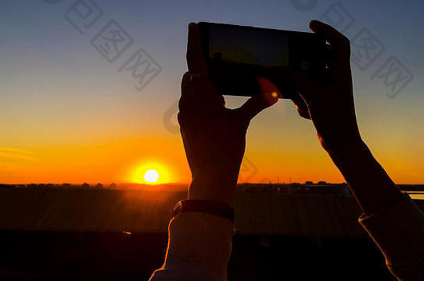 在城市里，女人用智能手机拍摄日落