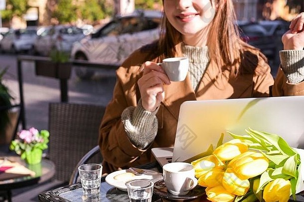 街上咖啡馆里一个漂亮的小女孩，桌上放着一台电脑。在咖啡馆吃早餐，远距离工作，<strong>自由</strong>职业者。<strong>旅<strong>游</strong>概念。桌上有一束黄色的郁金香。