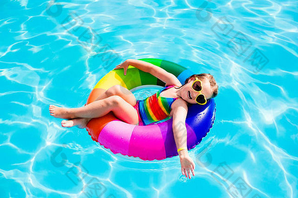在炎热的夏日，快乐的小女孩在室外游泳池里玩着五颜六色的充气戒指。孩子们学习游泳。儿童水玩具。儿童解放军