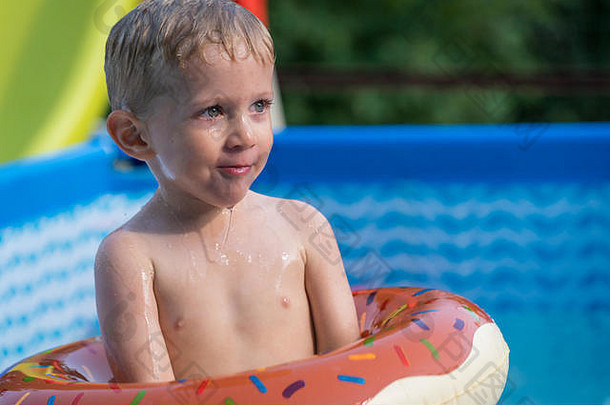 炎炎夏日，快乐的小男孩在室外游泳池里玩着五颜六色的充气戒指。孩子们学习游泳。儿童水玩具。