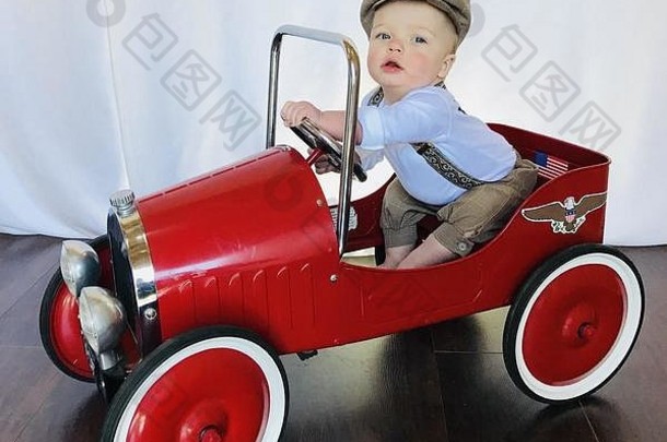 可爱的婴儿新闻男孩装玩古董兜售车可爱的婴儿穿棕色（的）如此短裤背带裤新闻男孩他坐在红色的车假装开车