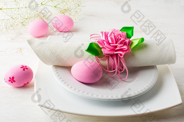 粉红色复活节餐桌，白色木质背景上有盘子、餐巾和粉红色装饰的复活节彩蛋