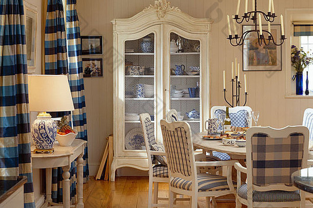 斯堪的纳维亚风格餐厅的白色玻璃前橱柜和蓝色 绿松石窗帘，配有白色木桌椅