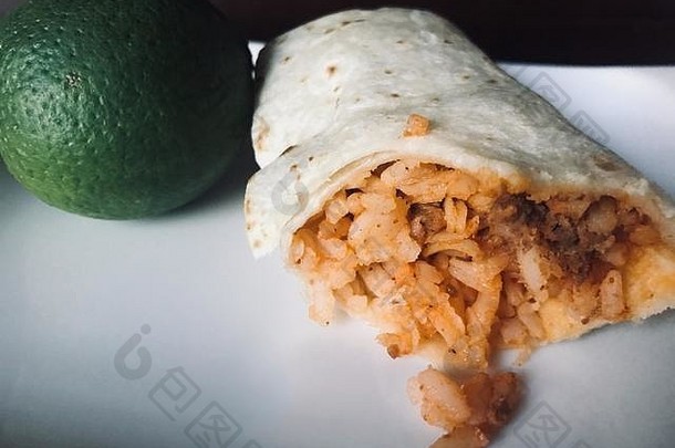 美味的墨西哥牛肉和米饭煎饼摆在白色盘子上，旁边放着绿色的酸橙
