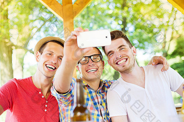 三个快乐的朋友在酒吧花园喝酒，用智能手机自拍