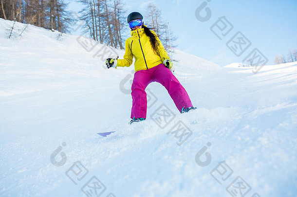 戴着头盔和滑雪板面具的女运动员的照片，拍摄于有树木的雪坡上
