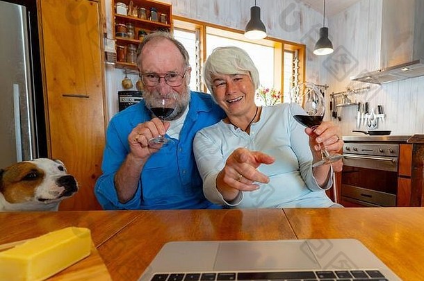 COVID-19保持连接和希望的概念。快乐的老年夫妇用葡萄酒视频在笔记本电脑上给朋友打电话或与家人在线聊天庆祝eas