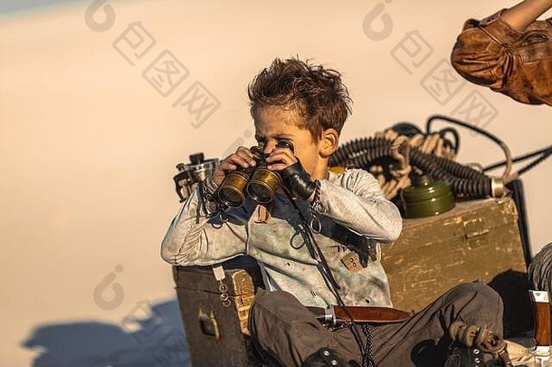 帖子世界末日英雄男孩双筒望远镜在户外沙漠死荒地背景英雄战士孩子破旧的衣服坐着营望远镜生活世界末日概念