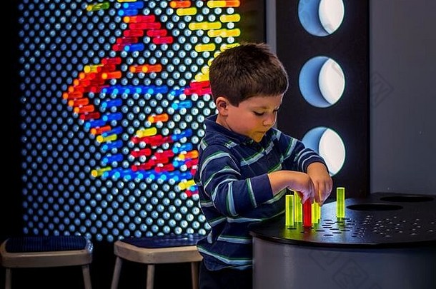 一个小男孩玩着彩色的亚克力钉和一个发光的格子，用颜色和光线来创造图案和形状