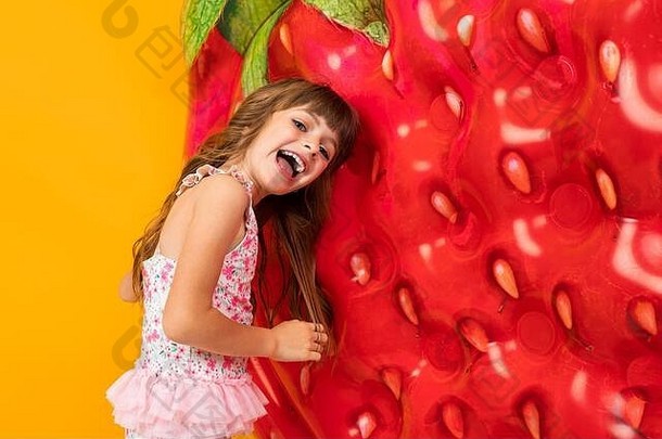 一个穿着泳衣的小<strong>女孩</strong>，在橙色背景上有一个草莓形状的气垫