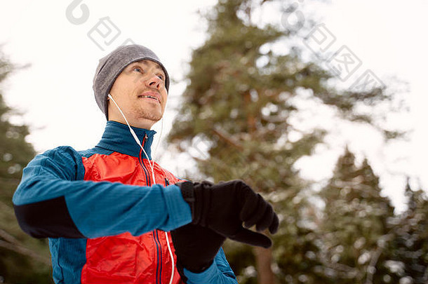 穿着保暖运动服戴着耳机的跑步者看着一个现代智能时钟
