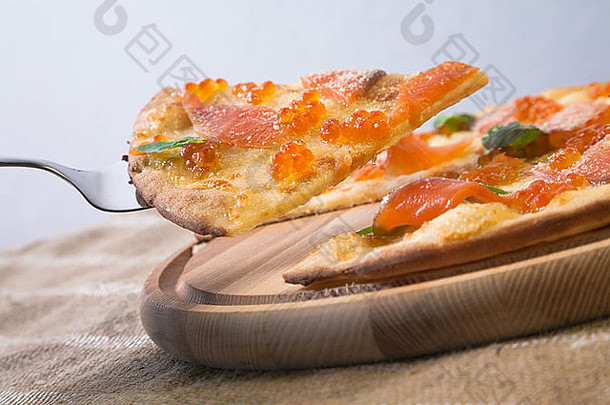 用钢制比萨切片器从木制比萨皮上切下鲑鱼和鲑鱼鱼子酱的比萨切片
