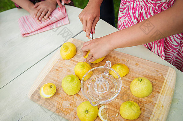 一个夏天在农场聚会的家庭。桌面砧板。把柠檬切碎并榨汁制成柠檬水的孩子。