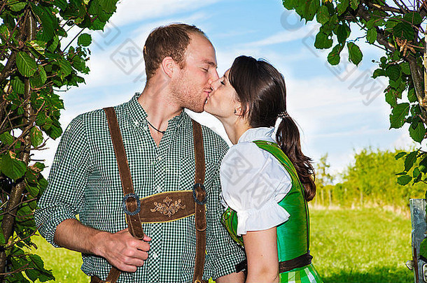 夫妇传统的巴伐利亚衣服站下面灌木接吻