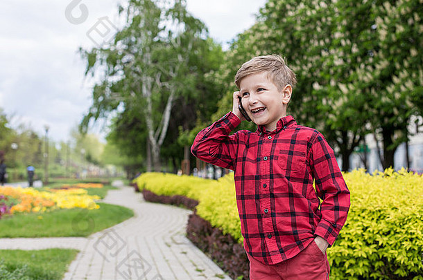 男孩红色的衬衫会说话的细胞电话在户外男孩微笑