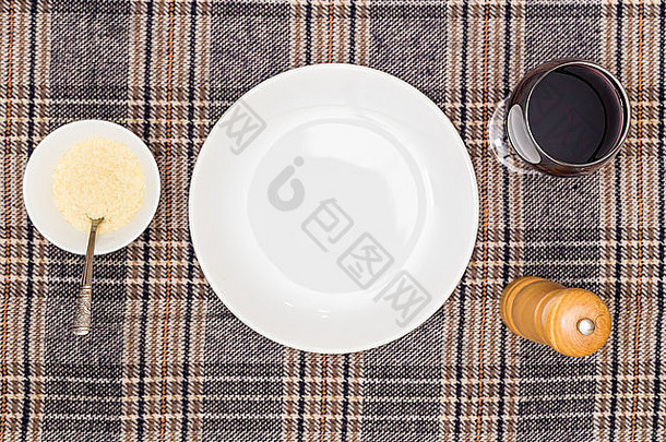 空的白色盘子里放着一杯葡萄酒和一碗帕尔马干酪。从上面看。