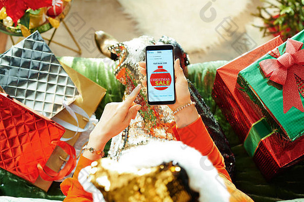 假期季节年轻的女闪耀黄金金片圣诞老人他电子商务电子邮件圣诞节出售优惠券智能手机坐着沙发上