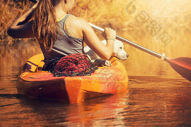 日落时，一位年轻女子在河上的独木舟上牵着一只小狗