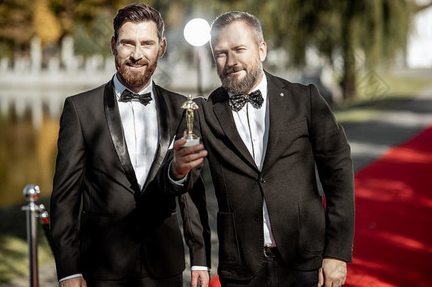 在室外红<strong>地毯</strong>上举行的颁奖典礼上，两位优雅的男士身着西装，扮演著名电影演员的肖像