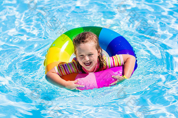 在炎热的夏日，快乐的小女孩在室外游泳池里玩着五颜六色的充气戒指。孩子们学习游泳