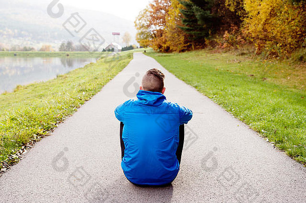 年轻的跑步者公园坐着沥青路径后视图