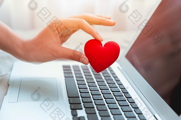 女孩手拿红心在笔记本电脑键盘上进行社交在线聊天，并通过互联网分享鼓励，共同对抗COVID-19病毒。