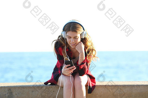 海滩上一个快乐的少女在智能手机上听音乐的前视图肖像