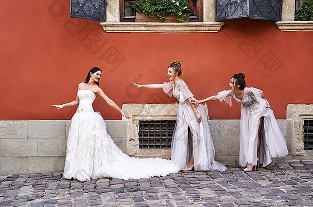 美丽的新娘和伴娘穿着华丽、优雅、时尚的浅灰色银色落地礼服，在古老美丽的欧洲城市里，在一个充满乐趣的夜晚