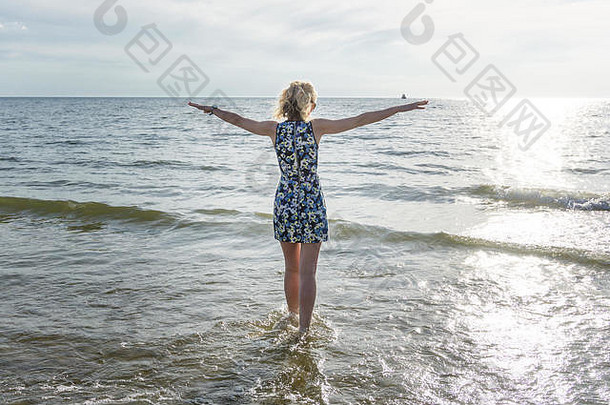 夏天，穿着短裙的快乐年轻女子在蓝天下的海滩上跳舞