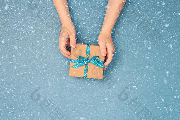 孩子们手里拿着一个用<strong>牛皮纸包装</strong>的礼品盒，用蓝灰色背景上的圆点蓝丝带系着。俯视图，放置文字。假日概念。
