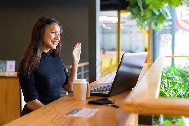 快乐的年轻美丽的亚洲女商人坐在咖啡馆里远距离视频通话