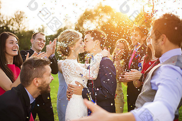 在绿色阳光公园，新婚夫妇和他们的朋友在婚礼派对上洒满五彩纸屑的全幅肖像