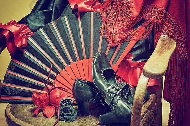 弗拉门戈舞的服装。黑色的鞋子、扇子、带流苏的红围巾和纸玫瑰躺在一把老式木椅上。