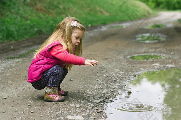 在森林里玩耍的金发小女孩，自然背景——向水中扔石头