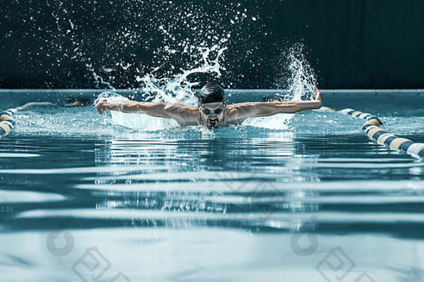 在游泳池里进行蝶泳的戴帽呼吸的运动员。那个年轻人。fitsport、游泳、游泳、健康、生活方式、比赛、训练、运动员、能量概念