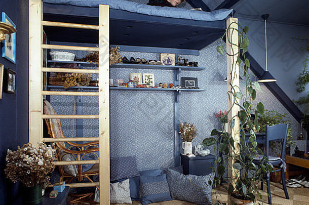 一个十几岁的男孩躺在70年代蓝色阁楼卧室的平台床上，地板上有<strong>蒲草</strong>垫子