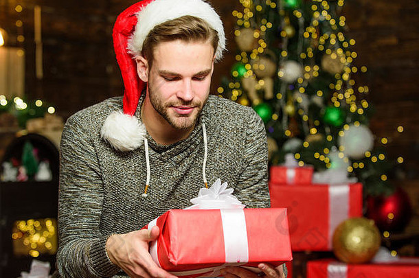 最好的礼物。快乐的家伙喜欢礼物。冬季购物销售。在家里庆祝新年。圣诞礼物。装饰圣诞树。最后的准备。圣诞节时间。快乐的男人戴着红色圣诞帽。