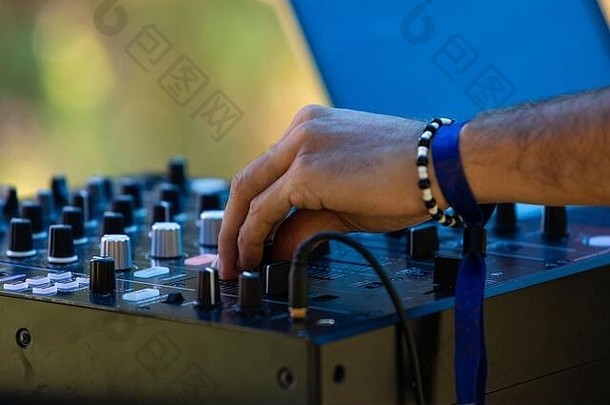 地球节上，一位电子音乐DJ戴着手镯，在模糊的绿色背景下转动CDJ混音器上的刻度盘