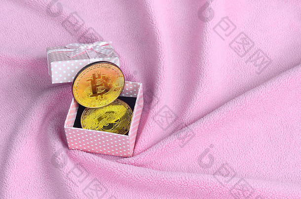 金色比特币放在一个粉红色小礼品盒中，小蝴蝶结放在柔软蓬松的浅粉色抓绒织物制成的毛毯上，毛毯上有大量