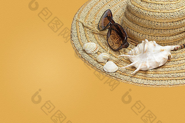 草帽、太阳镜和贝壳在照片的右侧。所有内容均位于黄色背景上，具有沙纹理。