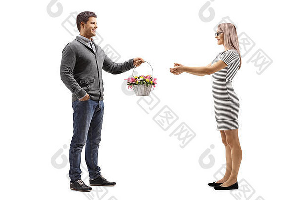 一名年轻男子向一名隔离在白色背景上的年轻女子赠送一篮鲜花的全长照片