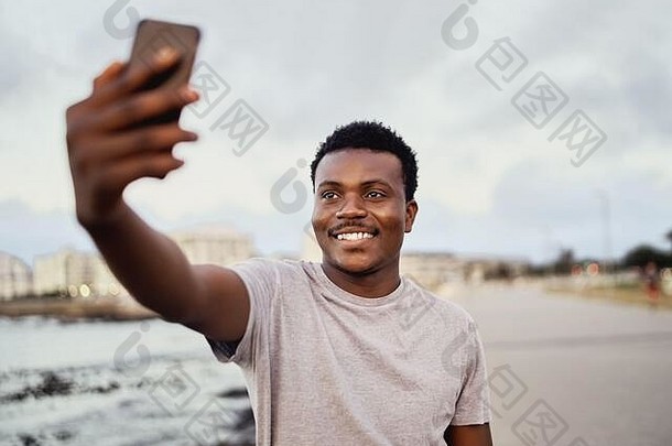 在城市背景下，一位面带微笑的年轻人在智能手机上自拍