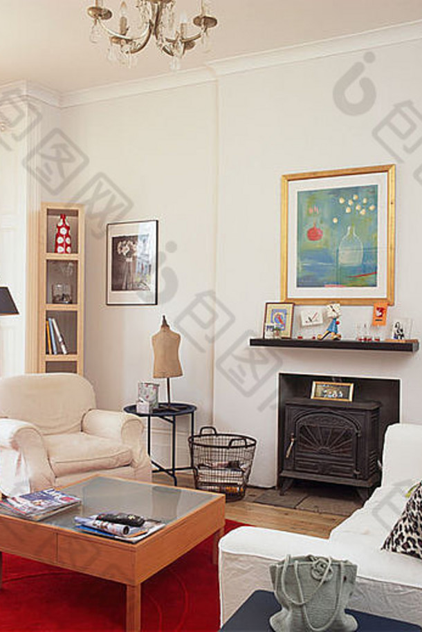 现代白色客厅中的白色扶手椅和沙发，壁炉前的红色咖啡桌位于墙上的大图下方